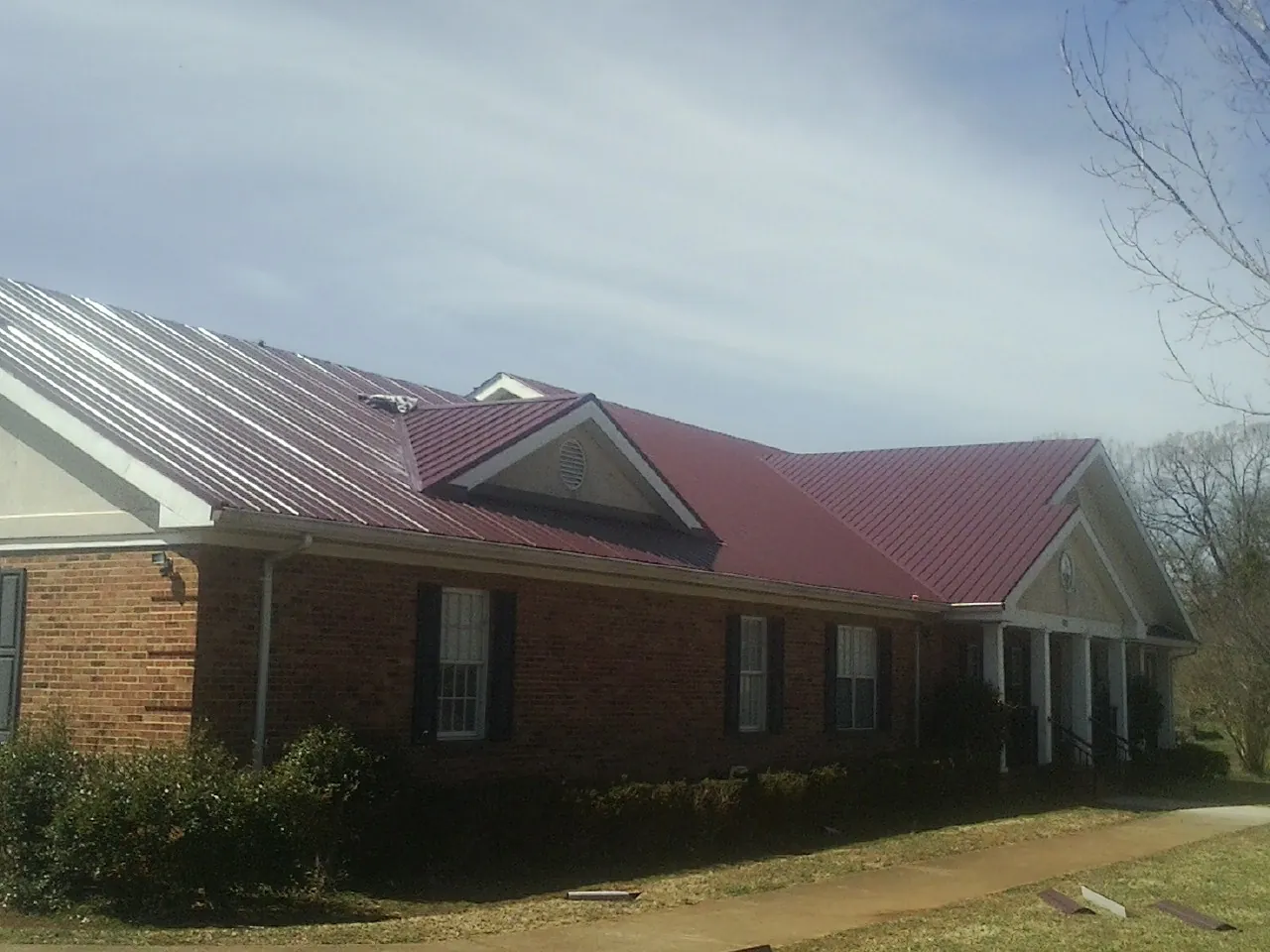 Red metal roof with gabled entries on a long brick building, from a Hail Damage Roof Repair job in New Boston