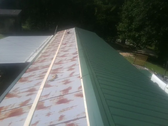 Old rusted panels beside newly installed green metal roofing — Wind Damage Roof Repair by Roofing Brothers in New Boston