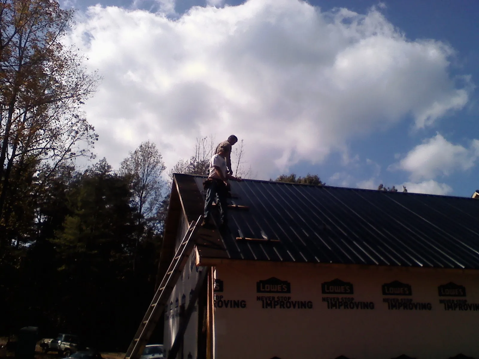 Roofer fastening dark metal panels high against a cloudy sky, from a Roof Inspection job in New Boston